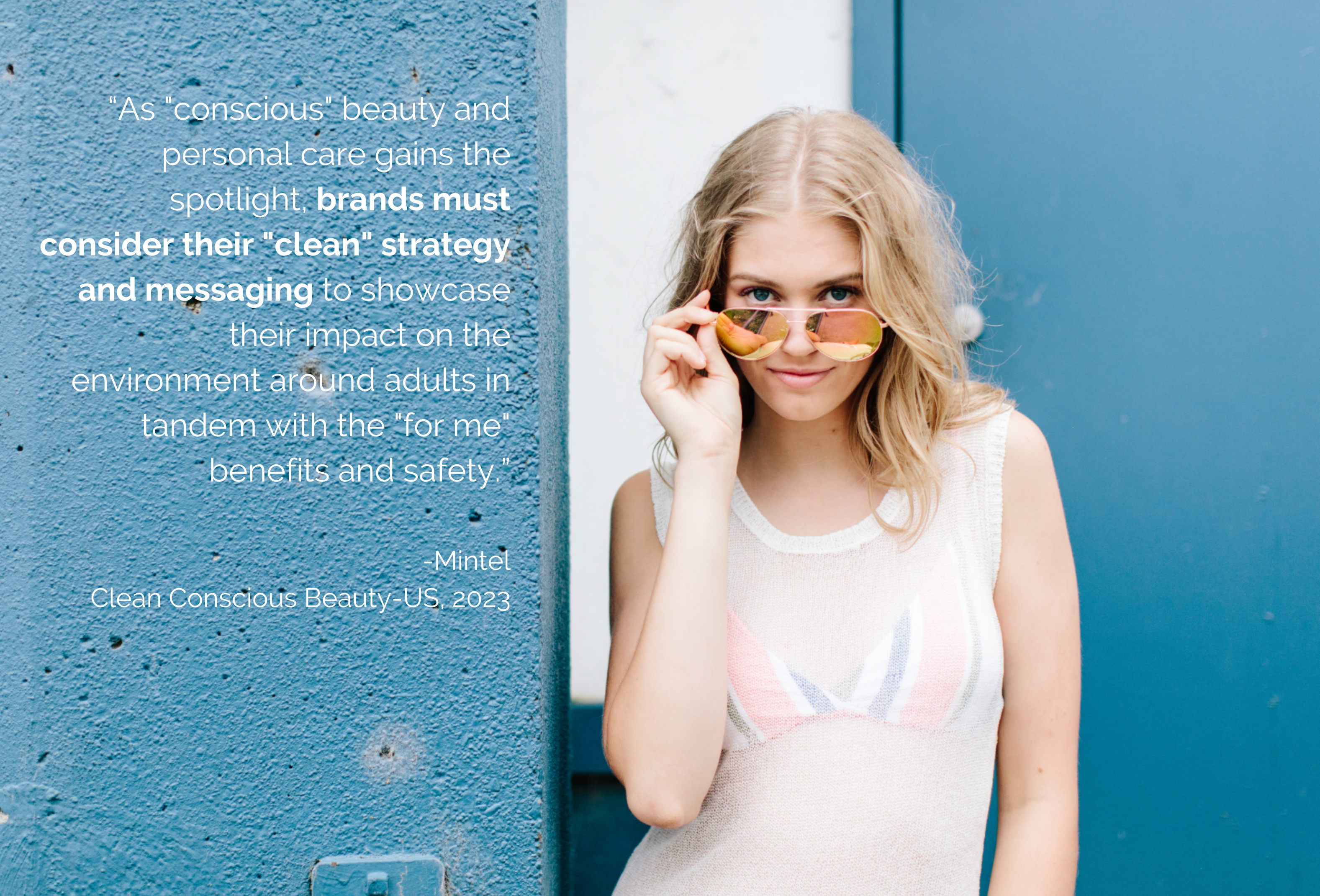 Woman at the beach, looking over her sunglasses while standing against a blue wall