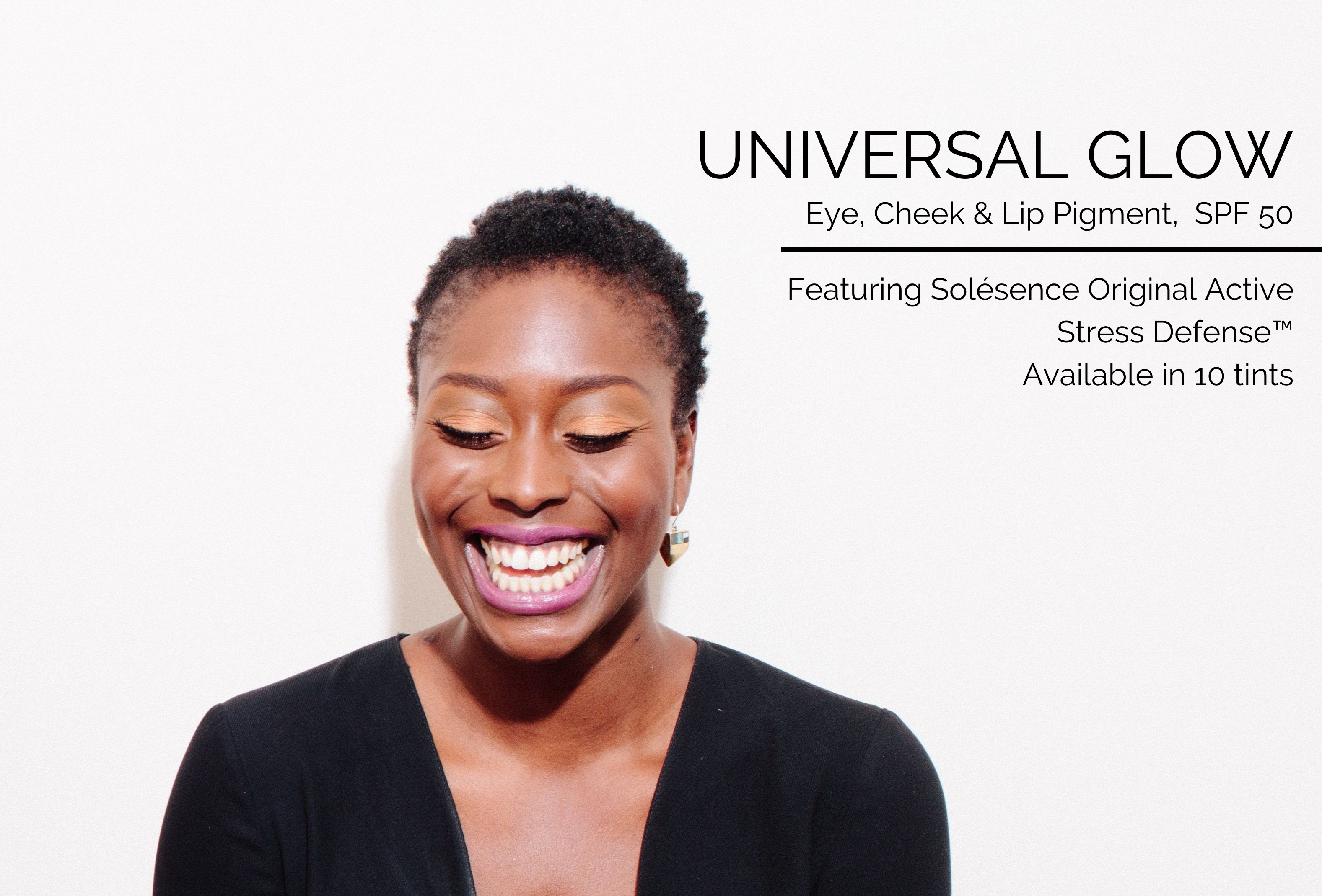 Woman wearing a black top, standing against a white wall while laughing