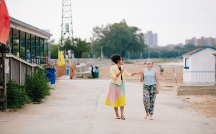 Two women walking on a sidewalk and eating popsicles.