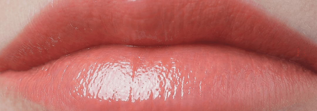 Two lips on a woman's face with orange lipstick on them.
